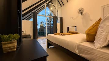 A modern bedroom with a bed, a bedside table, a potted plant, a fan, and a view of the outdoors.