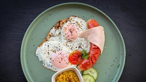 A plate with a fried egg, tomato slices, cucumber, and a small bowl of yellow condiment. - Tera Ella Boutique Hotel by SANS (Ella)