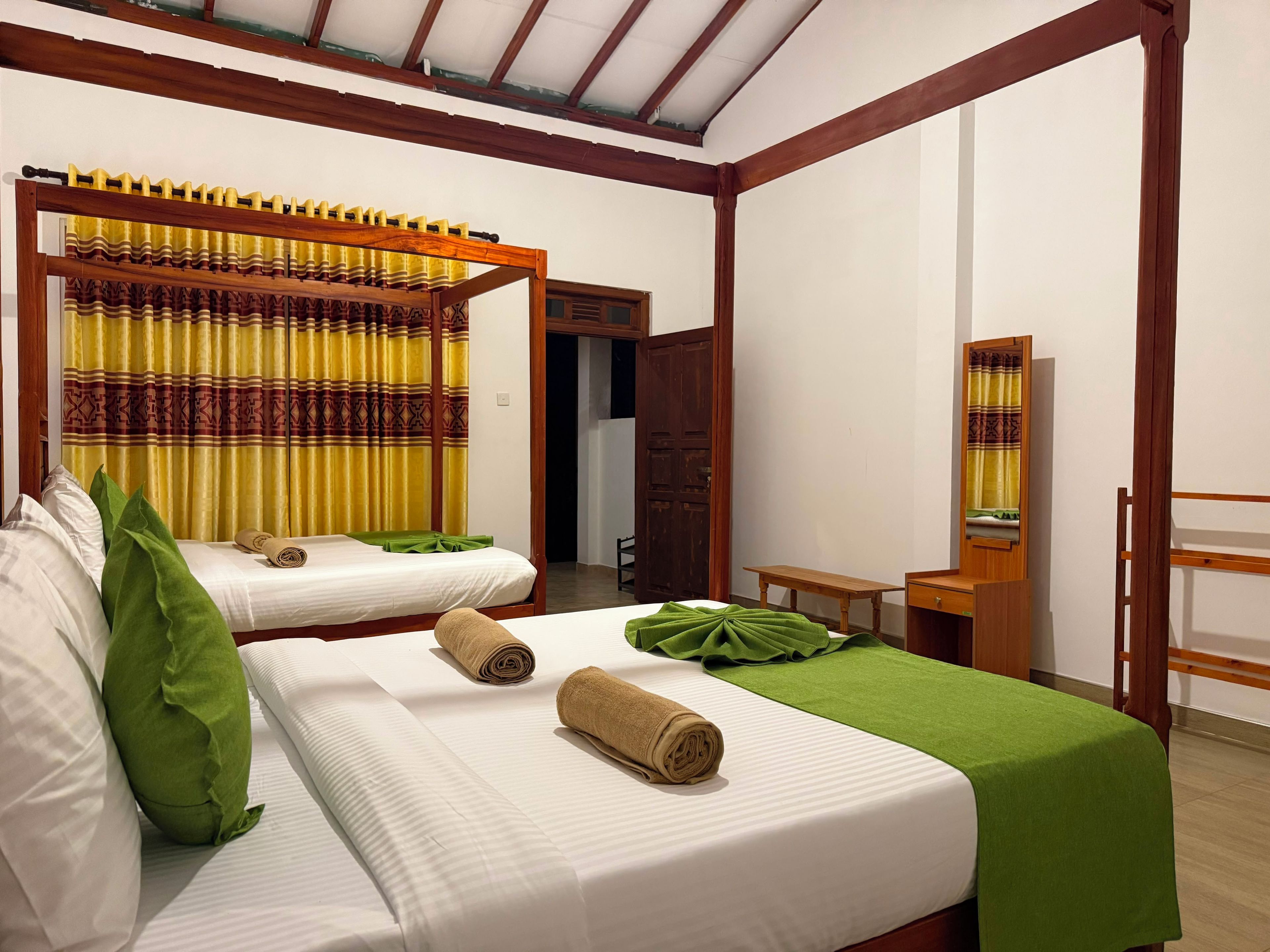 A hotel room with two beds, a wooden bench, a small table, and a mirror.