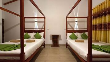 A room with two wooden bunk beds, each with a bedside table and lamp, and green pillows.