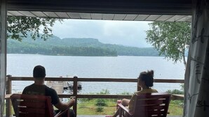 Twee personen zitten aan een tafel met uitzicht op een meer en heuvels.