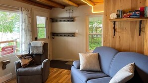 Een gezellige woonkamer met een blauwe bank, een leren fauteuil en houten planken met boeken en spellen.