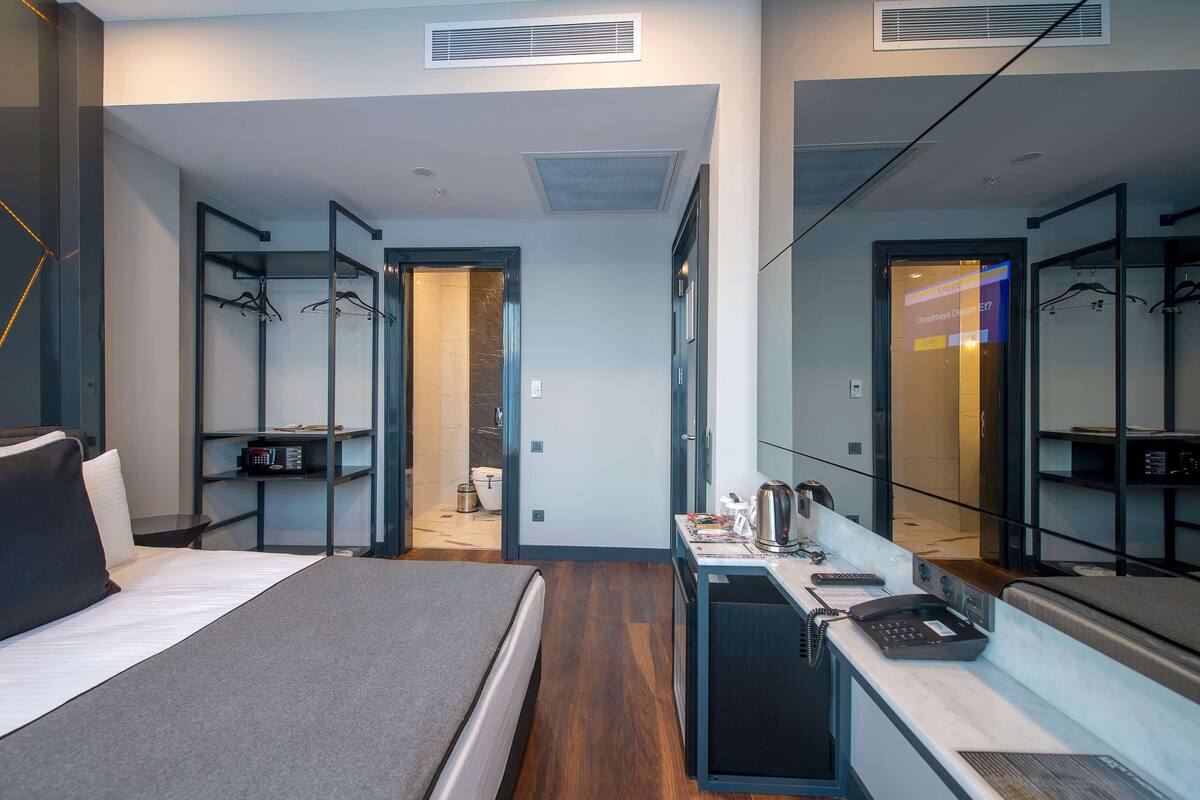 A modern hotel room with a bed, a desk with a telephone, and a mirror.