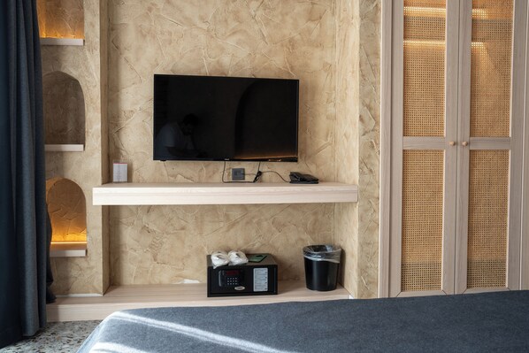 A modern room with a flat-screen TV mounted on a textured wall, a small shelf with a remote control, a microwave, and a trash bin.