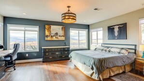 Ein Schlafzimmer mit einem großen Bett, einem Schreibtisch und einer Kommode. Es gibt zwei Fenster und ein Bild an der Wand.