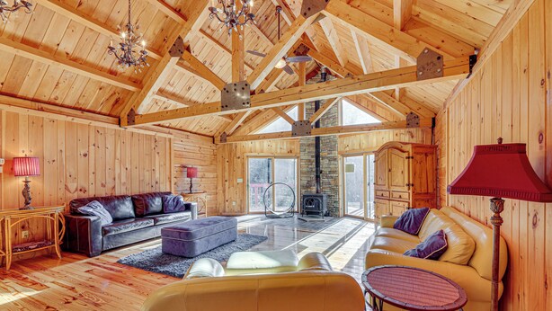 A spacious living room with wooden walls and a high ceiling, featuring a sofa, armchairs, and a small table. - 15 Mi to Snowshoe Resort: Cabin w/ Deck & Fire Pit (Dunmore)