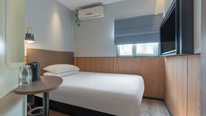 Een moderne hotelkamer met een bed, een televisie, een klein tafeltje met een lamp en een airconditioner.
