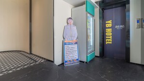 Een hotelentree met een digitaal bord, een receptiebalie en een lift.