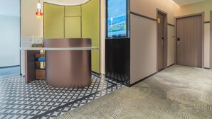 Een moderne hotel lobby met een receptiebalie, een digitaal scherm en een vloer met een patroon.
