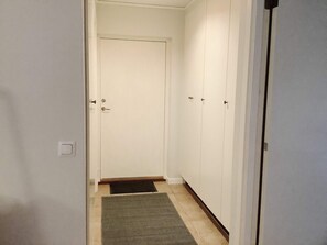 Een gang met een deur aan het einde, een deurmat en vloerkleed.