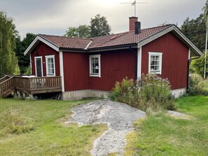 Een rood houten huis met een veranda, schoorsteen en een pad van stenen dat naar de ingang leidt.
