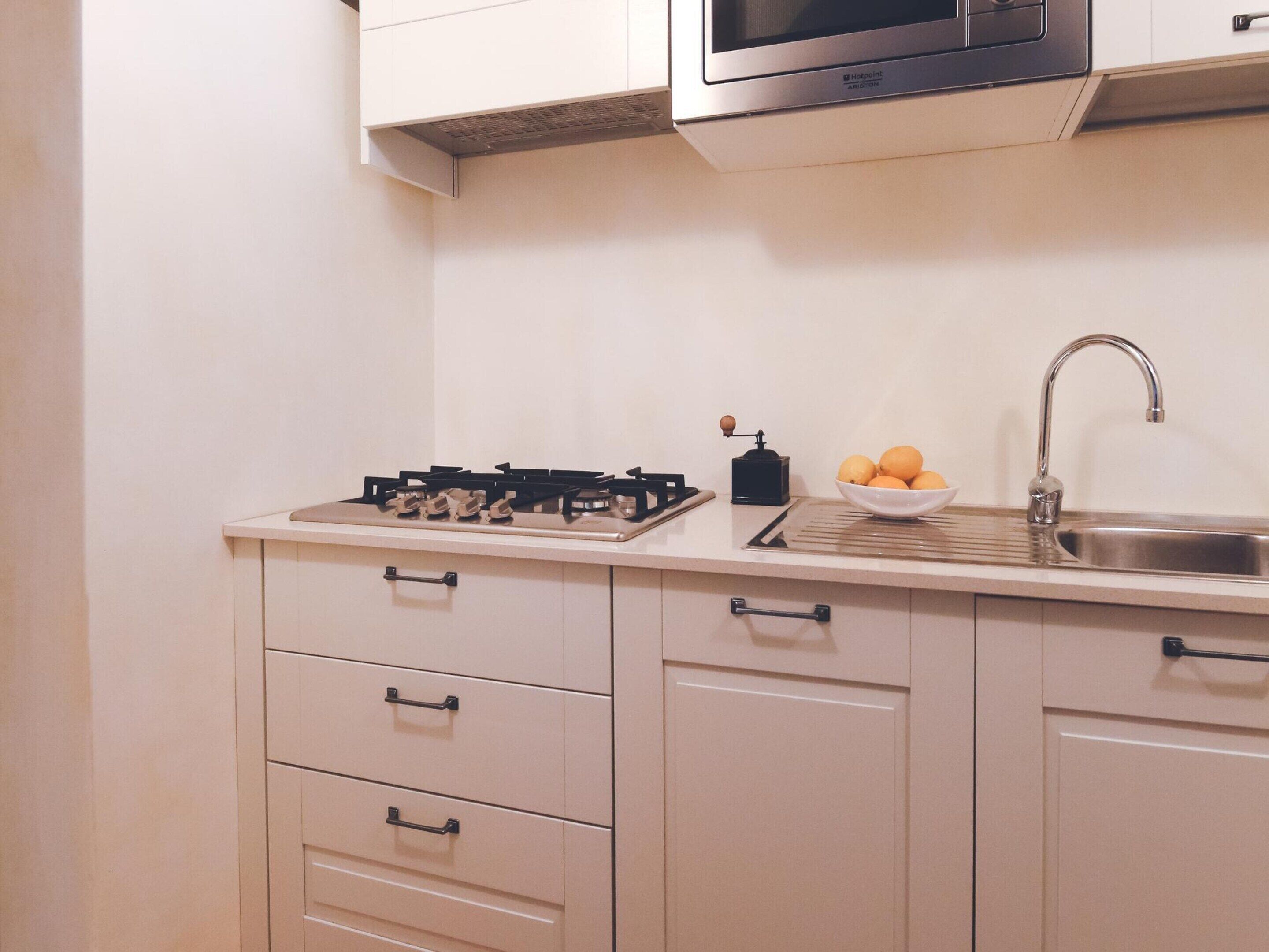 A kitchen with a gas stove, a sink, a microwave, and a bowl of oranges on the counter.