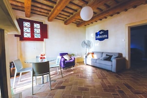 Una sala de estar con comedor, un sillón morado, un sofá y un ventilador.