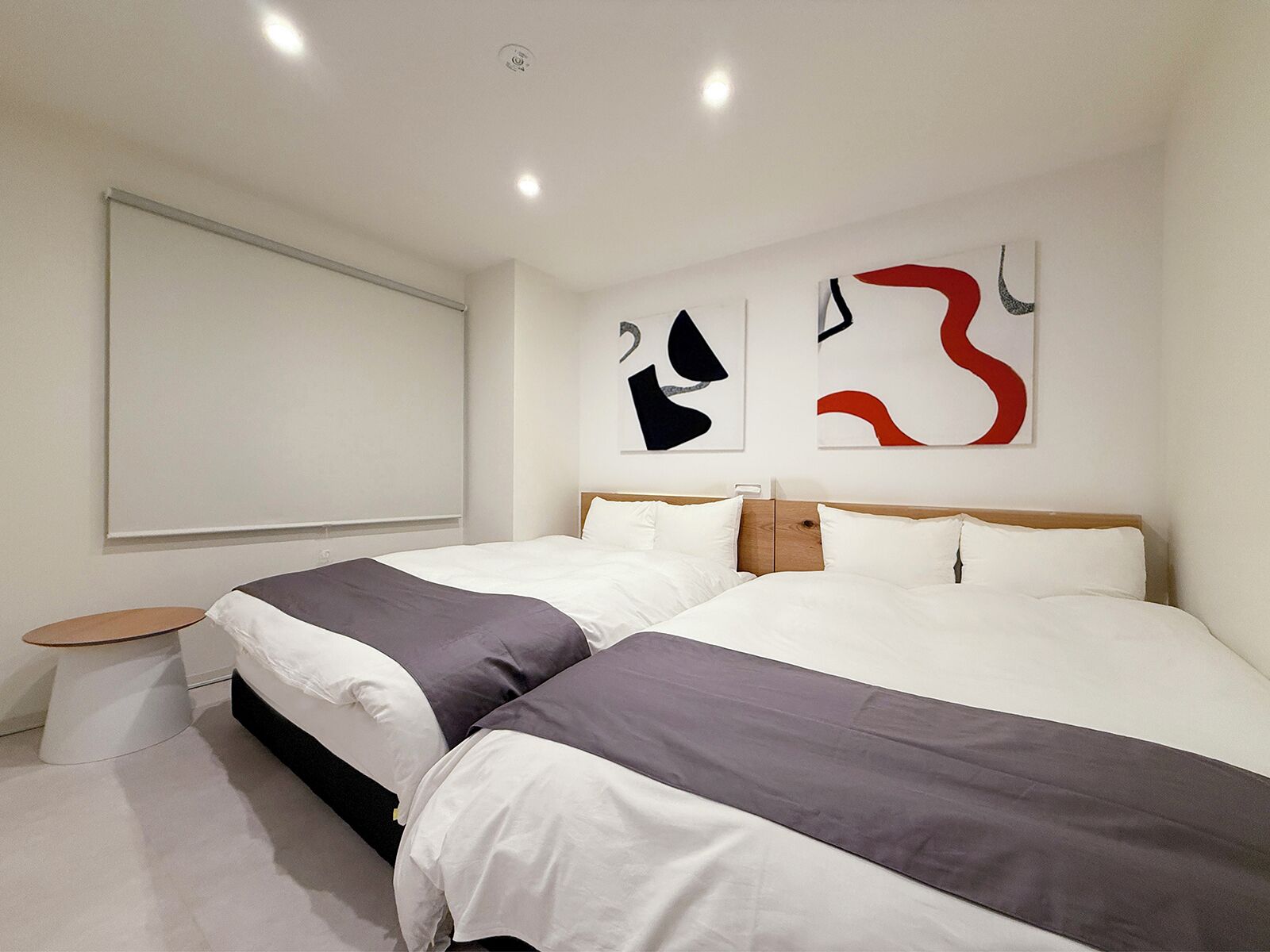 Et moderne hotelværelse med to senge, et lille rundt bord og abstrakt vægkunst.