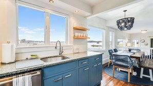 A modern kitchen with a large window, a built-in dishwasher, and a dining area with a round table and chairs. - Oceanfront Dock Escape ~ Kayaks & Paddleboards (Gloucester)