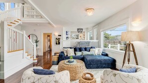 A spacious living area with a staircase, a sofa set, a coffee table, and a large window. - Oceanfront Dock Escape ~ Kayaks & Paddleboards (Gloucester)