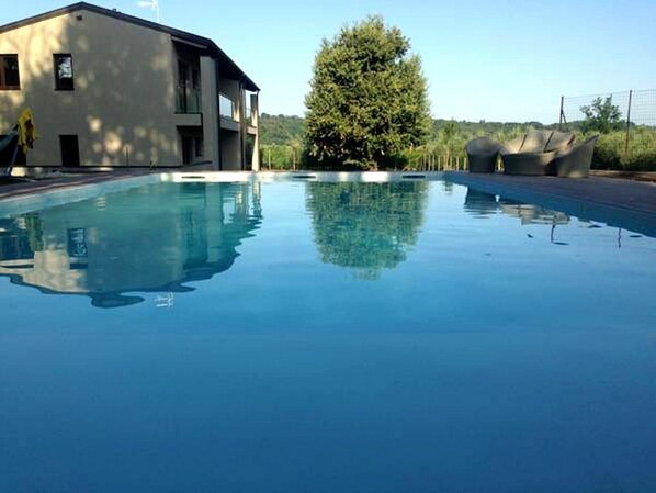 A swimming pool with a building and a tree in the background. - Apartment in Iseo With Pool (Cazzago San Martino)