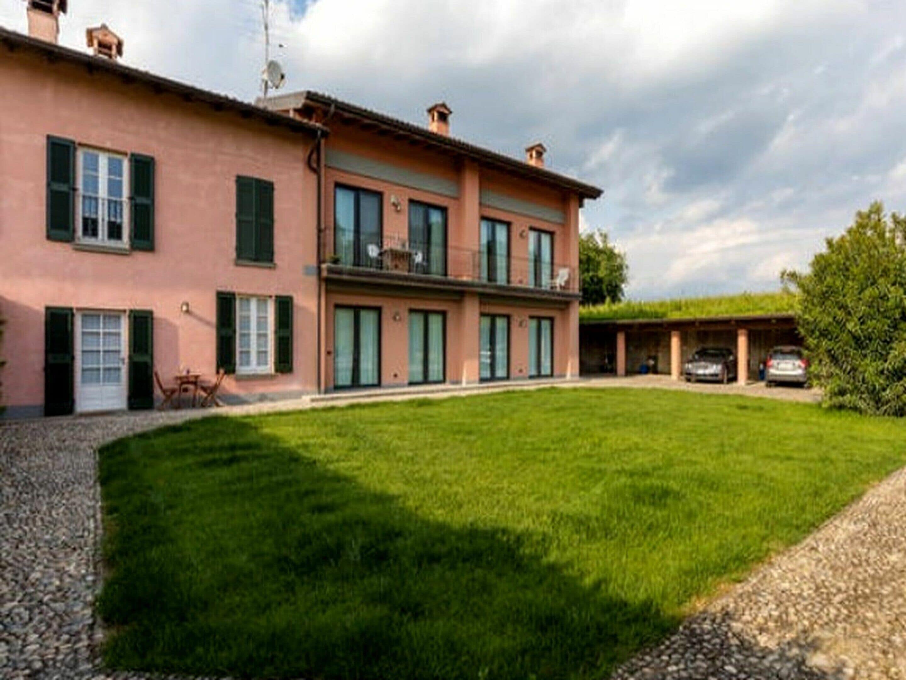 A two-story house with a large lawn, a covered carport, and a gravel driveway.