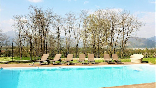A swimming pool with lounge chairs and a sun lounger, surrounded by trees and mountains in the background. - Apartment in Iseo With Pool (Cazzago San Martino)