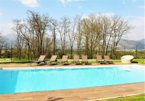 A swimming pool with lounge chairs and a sun lounger, surrounded by trees and mountains in the background. - Apartment in Iseo With Pool (Cazzago San Martino)