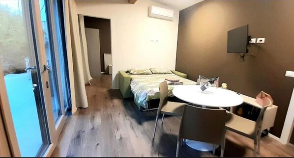 A hotel room with a bed, a round table with chairs, a TV mounted on the wall, and a sliding glass door leading to an outdoor area. - Apartment in Iseo With Pool (Cazzago San Martino)