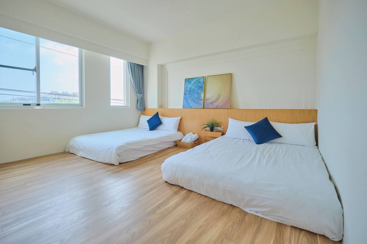 A hotel room with two beds, a wooden headboard, a window with a view, and a painting on the wall.