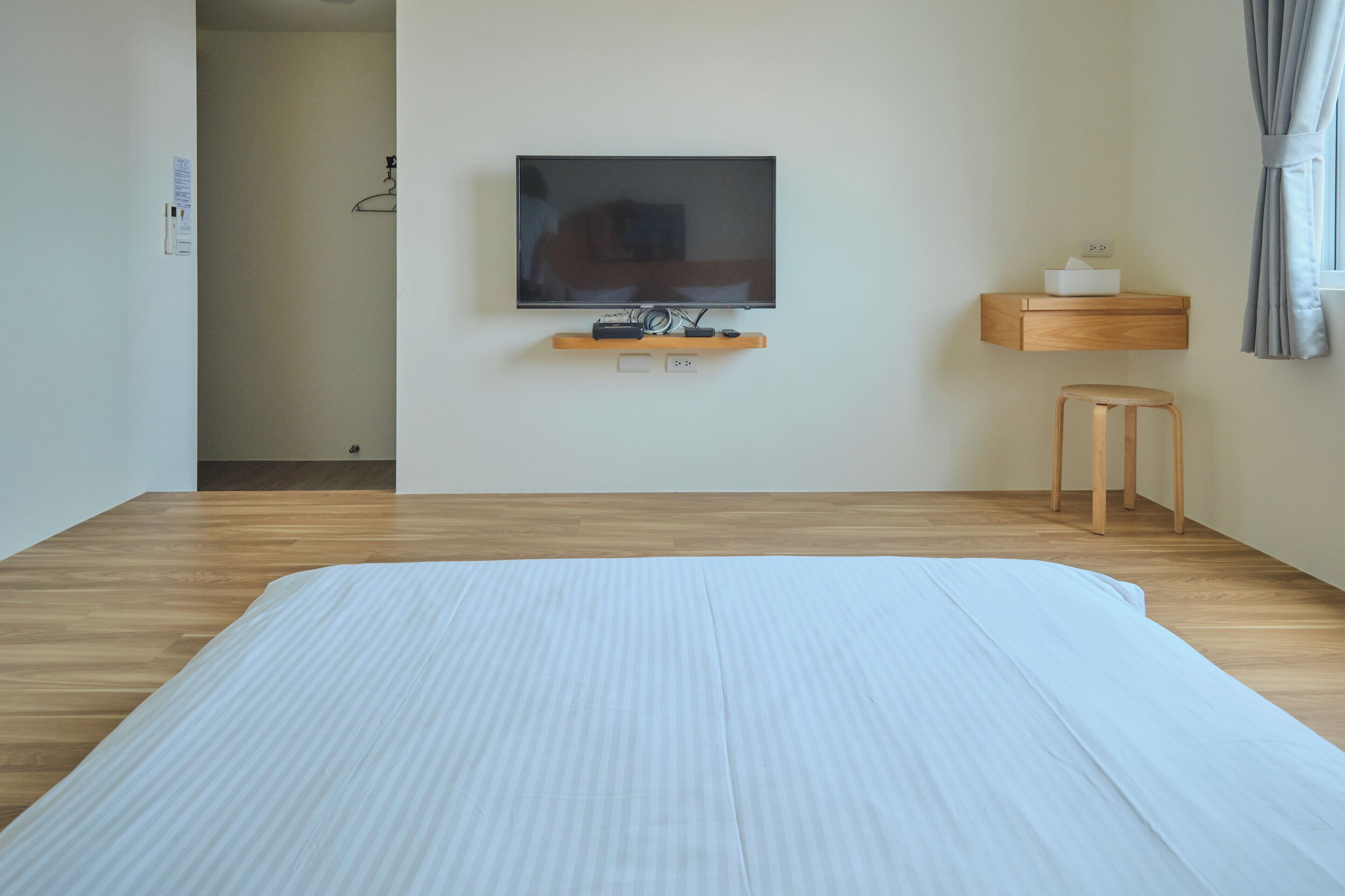 A hotel room with a large bed, a TV mounted on the wall, a wooden nightstand, and a small stool.