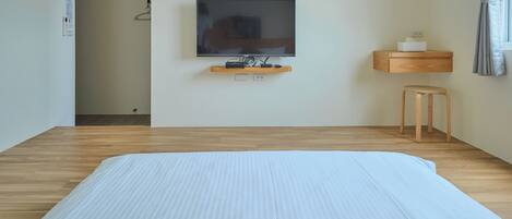 A hotel room with a large bed, a TV mounted on the wall, a wooden nightstand, and a small stool.
