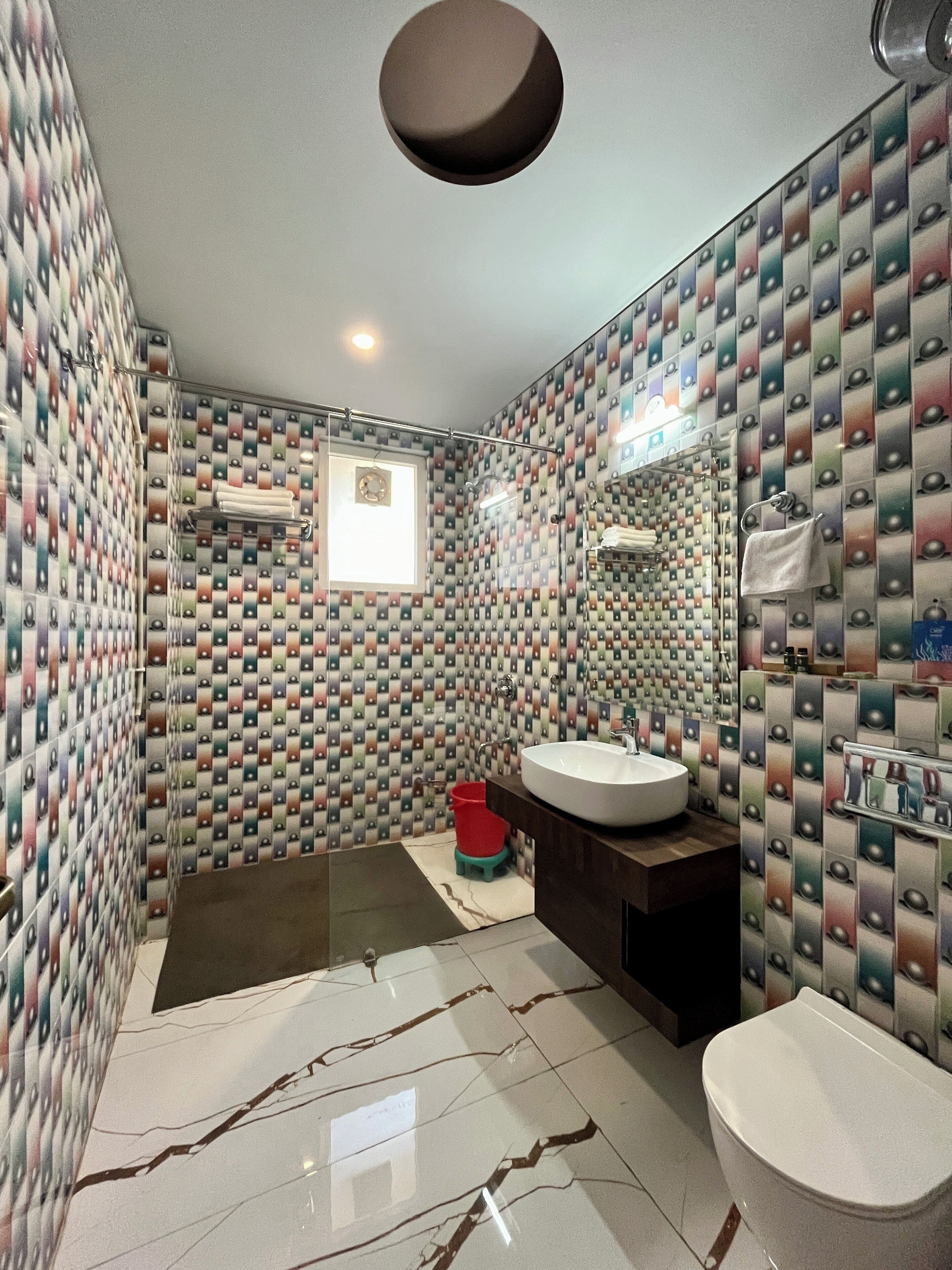 A bathroom with patterned walls, a sink, a toilet, and a shower area.