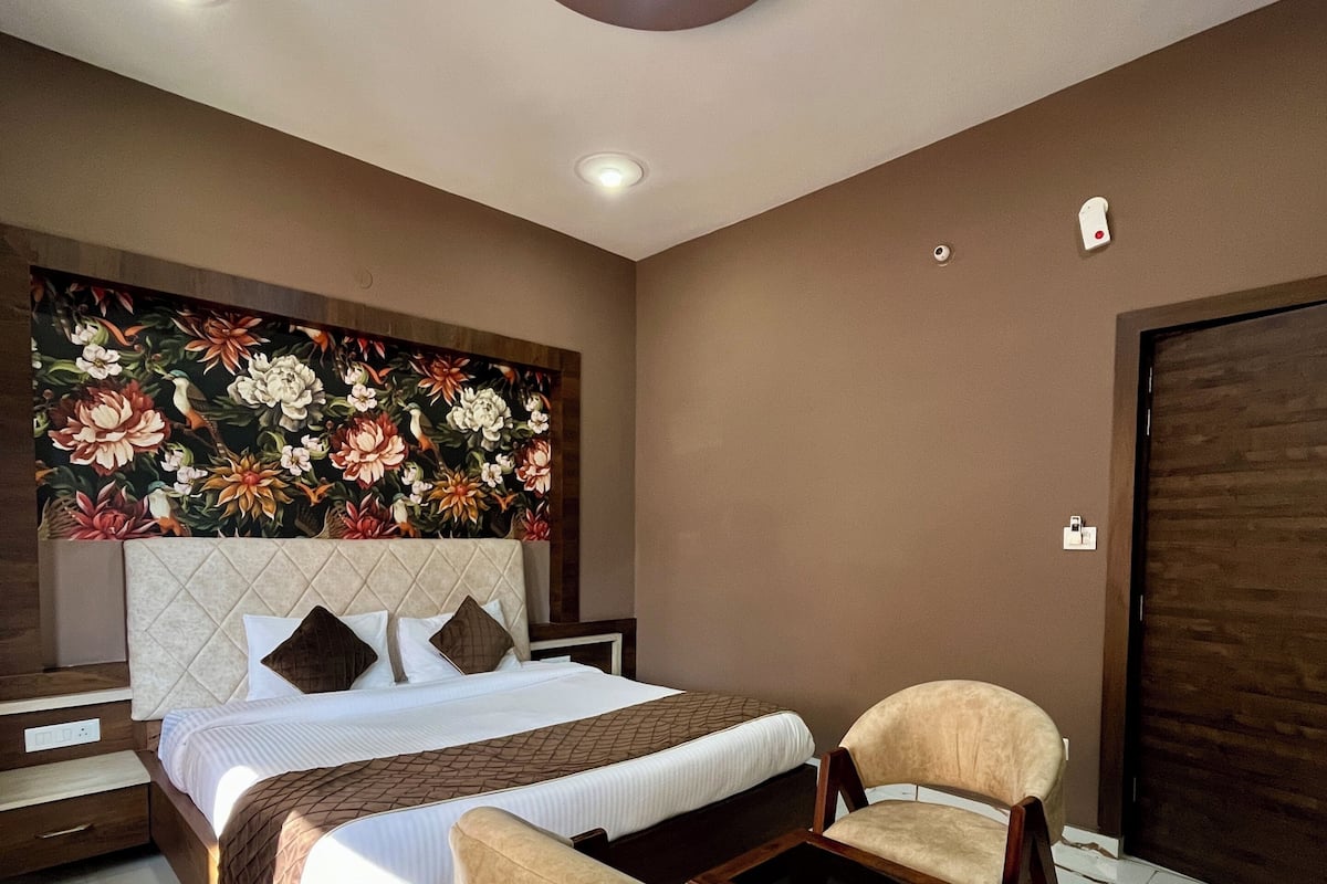 Habitación de hotel con cama, dos sillones, una mesita de noche, televisor montado en la pared y luz en el techo.