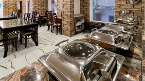 Un restaurante con pared de piedra, un área de comedor con sillas y una mesa, y estaciones de buffet con bandejas de metal.