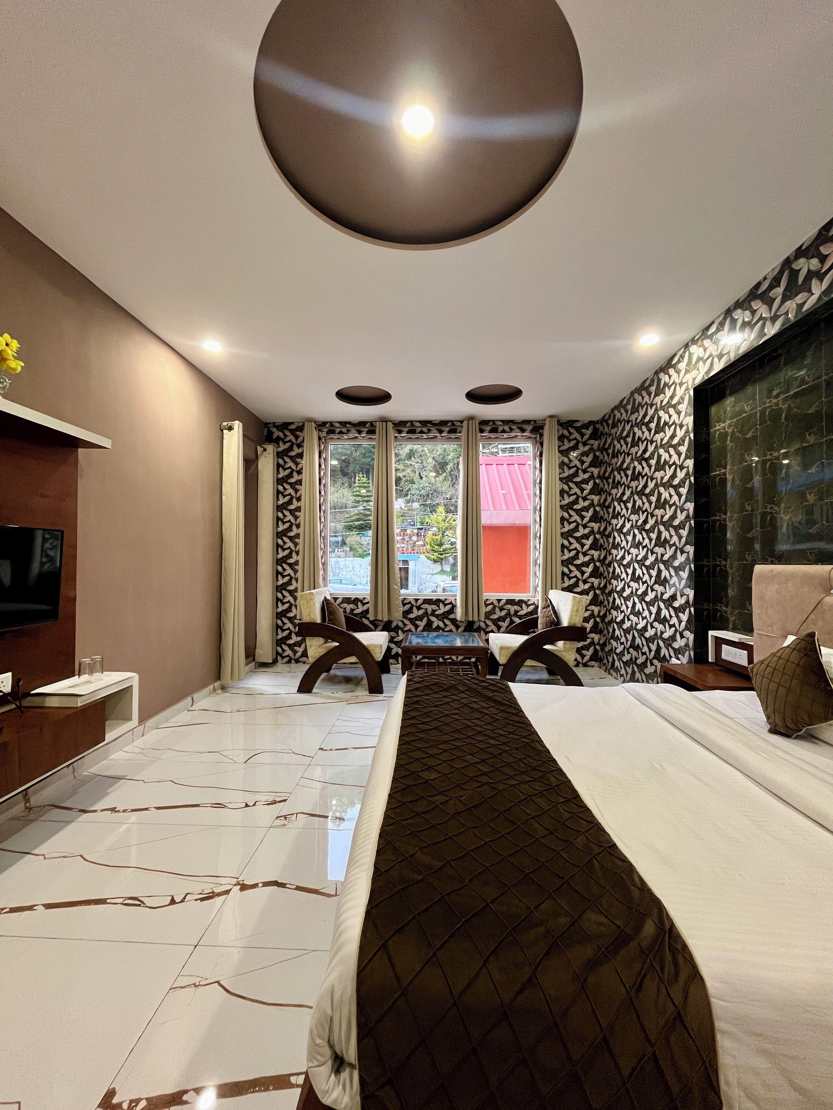A modern hotel room with a large bed, a flat-screen TV, a desk, and a view of the outside.