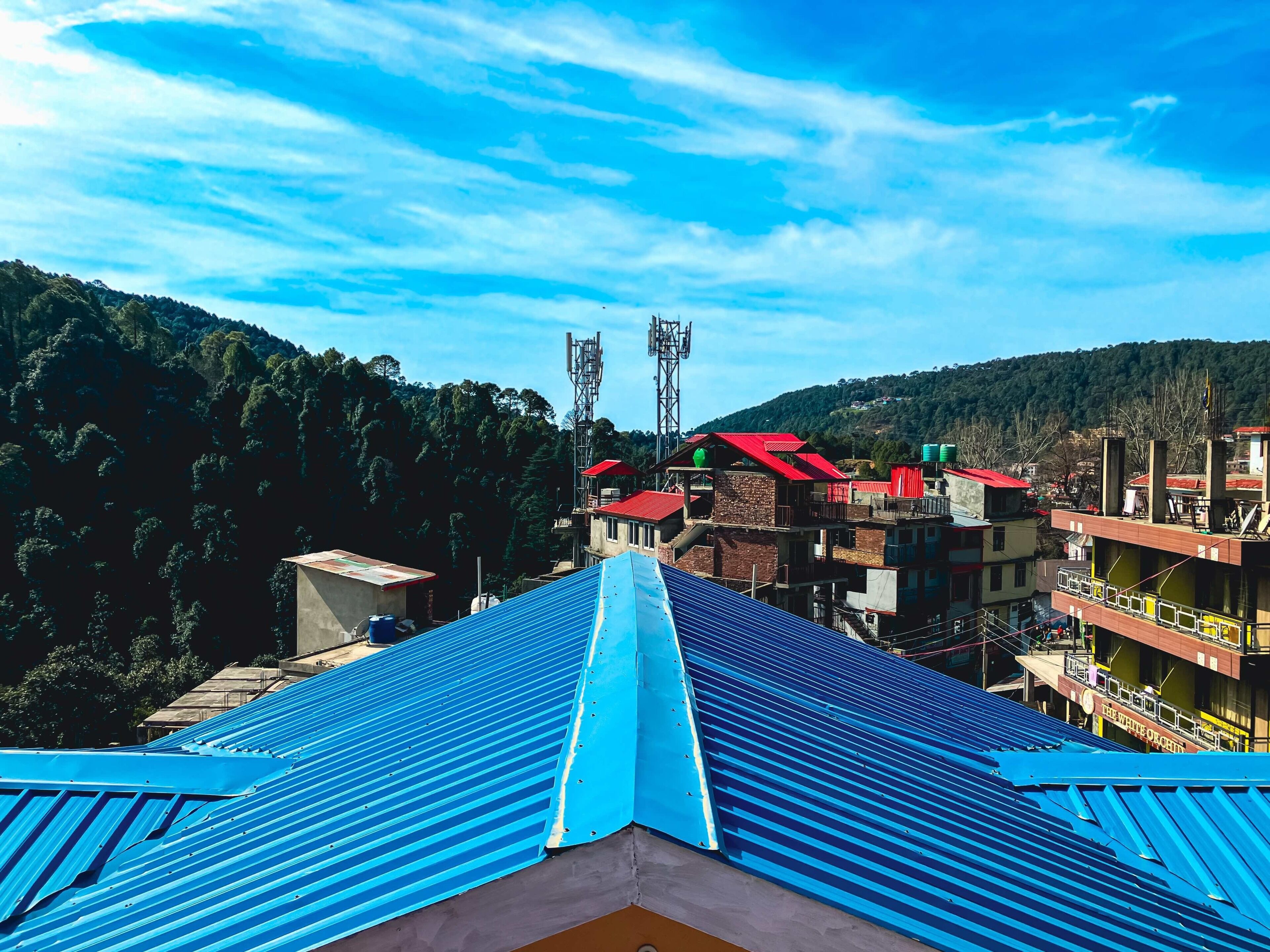 A view of a building with a blue roof, surrounded by other buildings and a forested hillside.