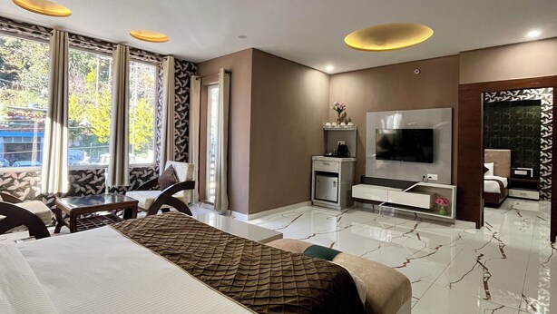 Una habitación de hotel moderna con una cama grande, un televisor de pantalla plana, un minibar y una zona de estar con vistas al exterior.