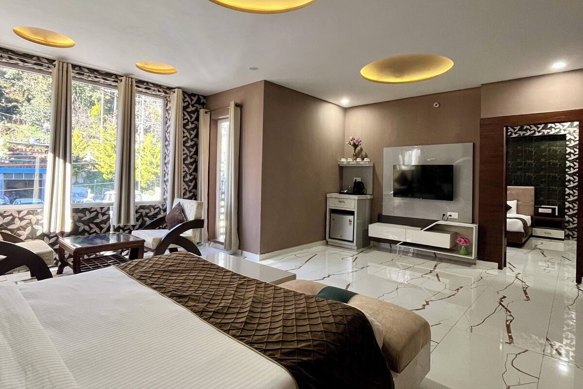 Una habitación de hotel moderna con una cama grande, un televisor de pantalla plana, un minibar y una zona de estar con vistas al exterior.