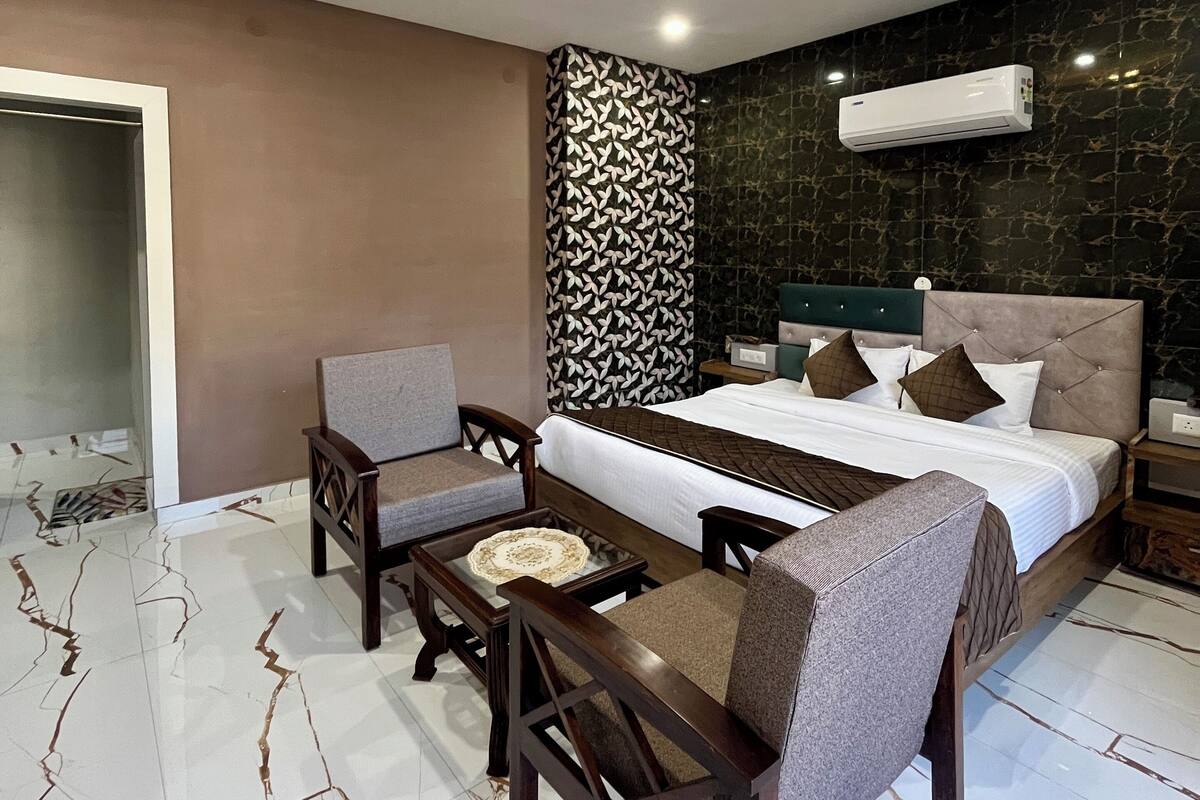 Una habitación de hotel moderna con una cama grande, dos sillones, una mesita y una lámpara en el techo.