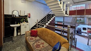 A modern living room with a sofa, a staircase, a sink, and a fire extinguisher. - Shivam Guest House (Faizabad)