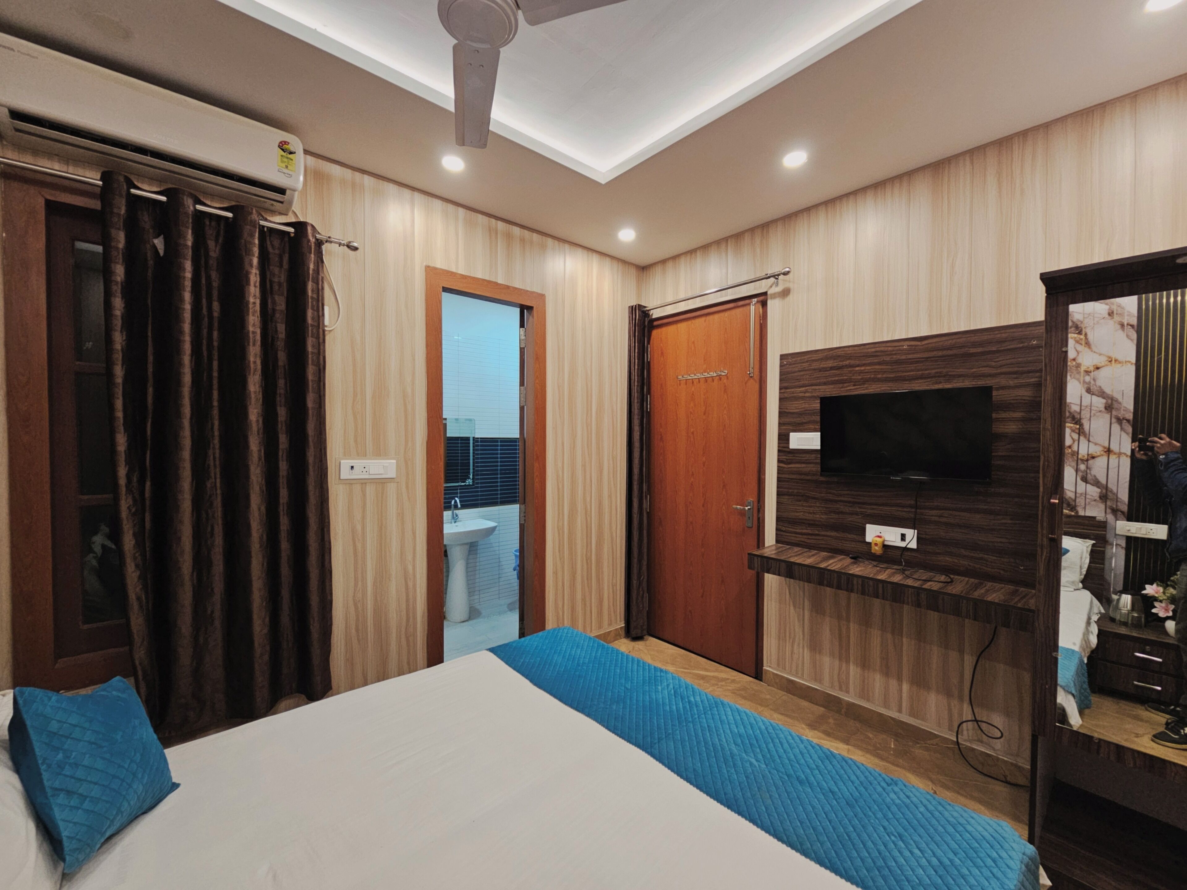 A modern bedroom with a bed, a TV mounted on the wall, a ceiling fan, and a wooden wardrobe.