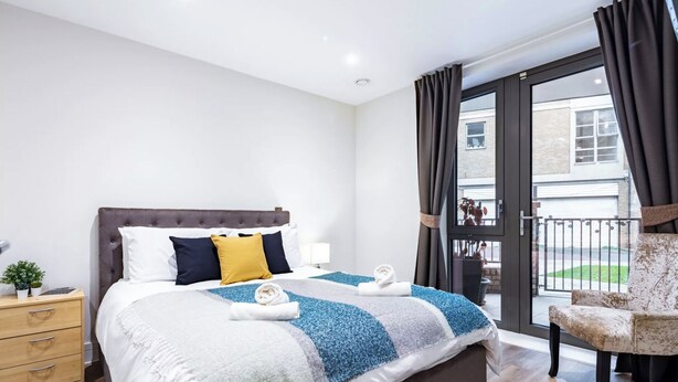 A modern bedroom with a large bed, a nightstand, a chair, and a view of the outside. - Cosy 1-bed flat in heart of London Bridge (London)