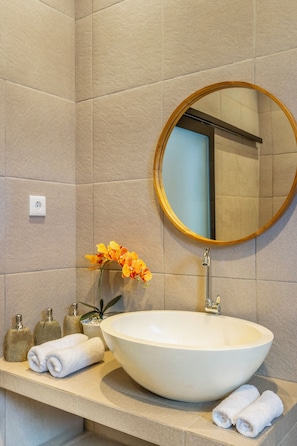 A bathroom with a large white sink, a round mirror, and a vase with flowers.