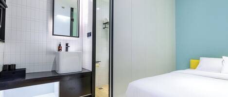 Una habitación de hotel moderna con una cama grande, un baño con espejo y suelo de madera.