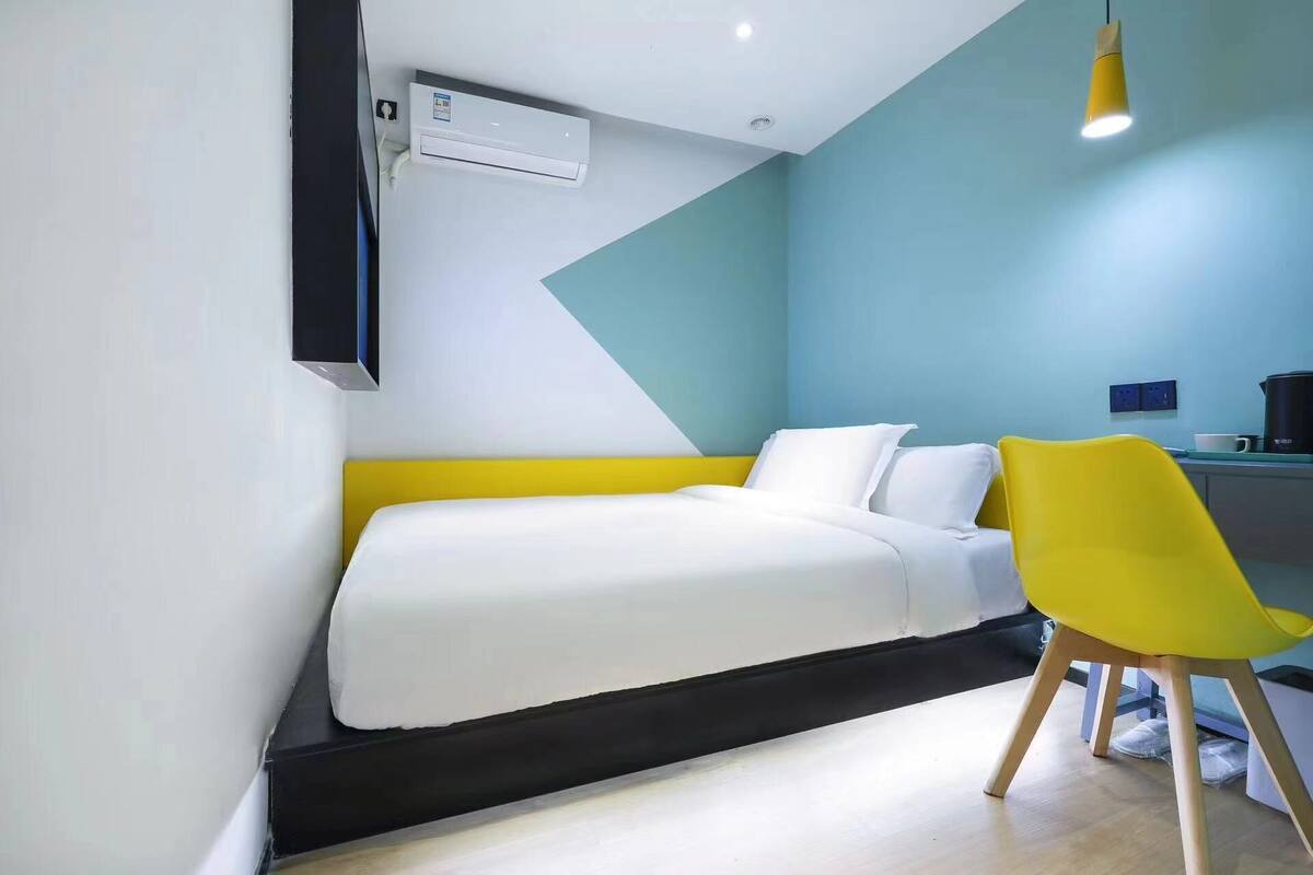 A modern hotel room with a bed, a yellow chair, and a coffee machine.