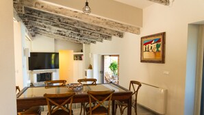 A dining area with a glass table, wooden chairs, a television, and a painting on the wall. - Villa Onda Celeste - Sardinia Unlimited (Costa Paradiso)