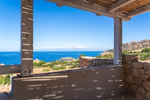A coastal view from a wooden pergola overlooking the sea and a rocky hillside.