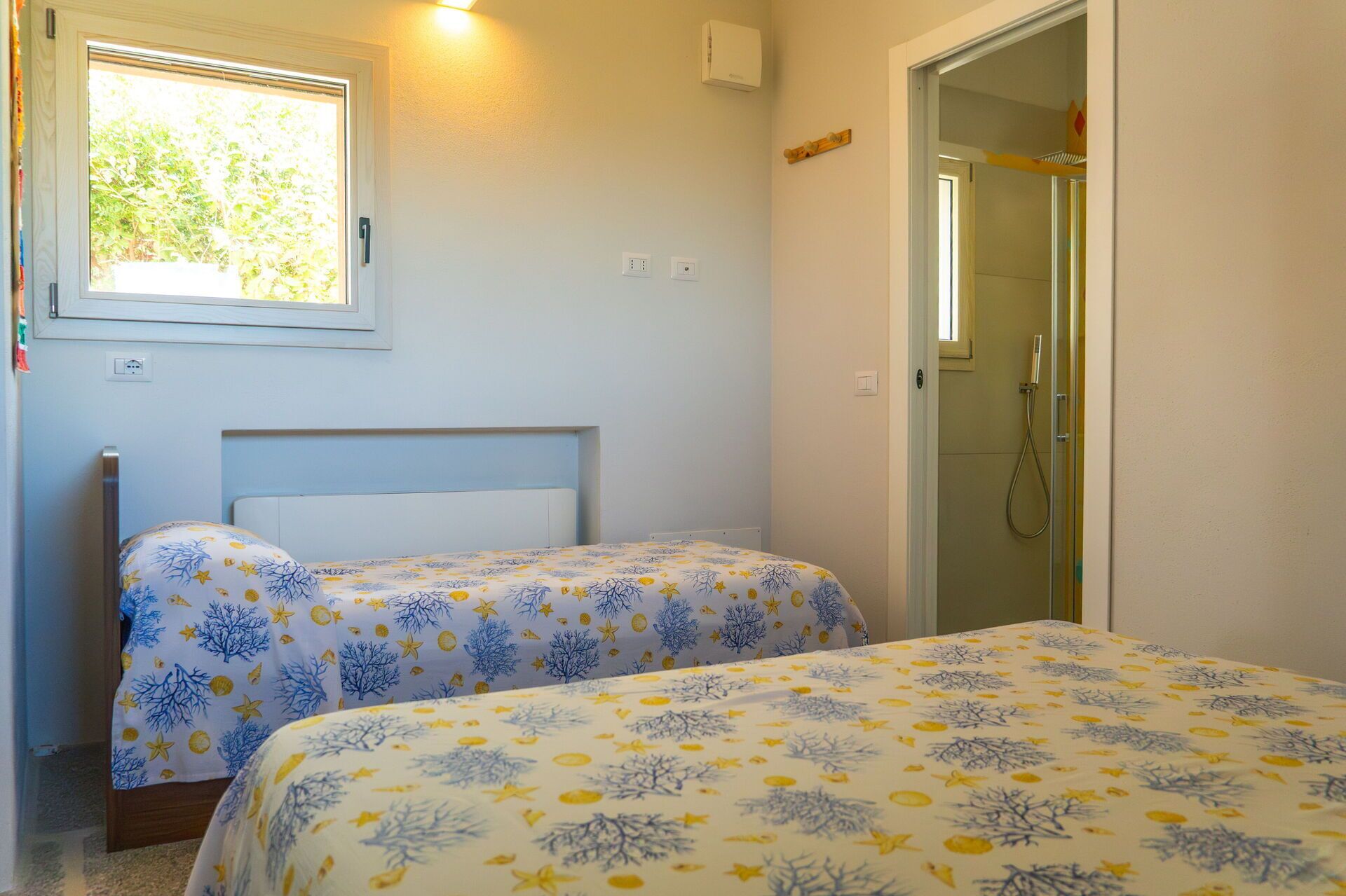 Ein Zimmer mit zwei Betten, einem Fenster, einer Dusche und einer Tür.