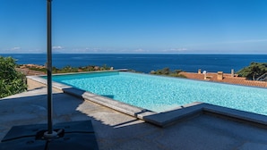 A clear blue swimming pool with a view of the ocean and a tiled roof in the background. - Villa Onda Celeste - Sardinia Unlimited (Costa Paradiso)