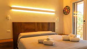 A neatly made bed with white linens and towels, a wooden headboard, and a wall-mounted light fixture. - Villa Onda Celeste - Sardinia Unlimited (Costa Paradiso)