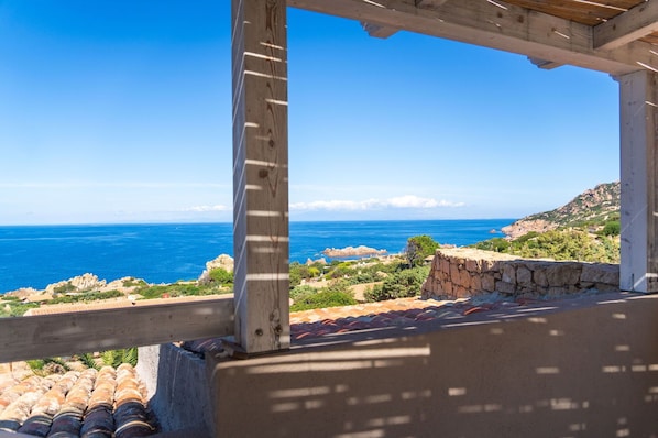A coastal view from a wooden balcony with a stone wall and tiled roof.