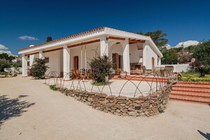 A white villa with a covered patio, stone wall, and outdoor furniture.