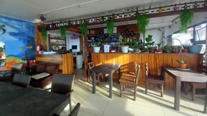 Un restaurante con mobiliario de madera, una zona de bar con botellas y plantas en macetas.